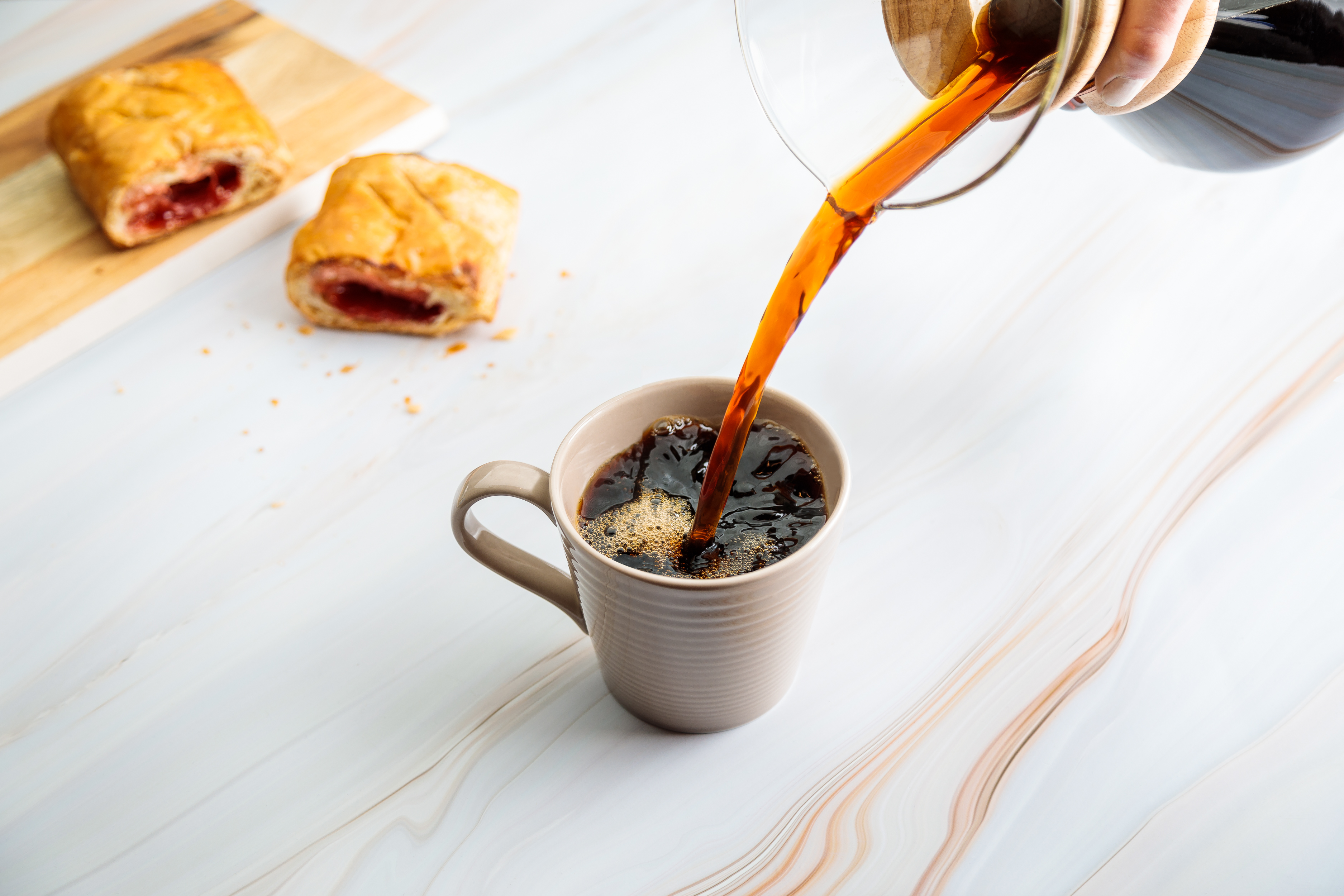 Coffee photography showing freshly brewed coffee being poured into a mug, styled with pastries for café menu and food marketing use.