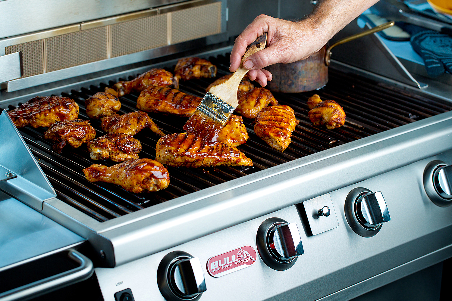 Process-focused food photograph of chicken being brushed with sauce on a grill, capturing cooking action for restaurant marketing.