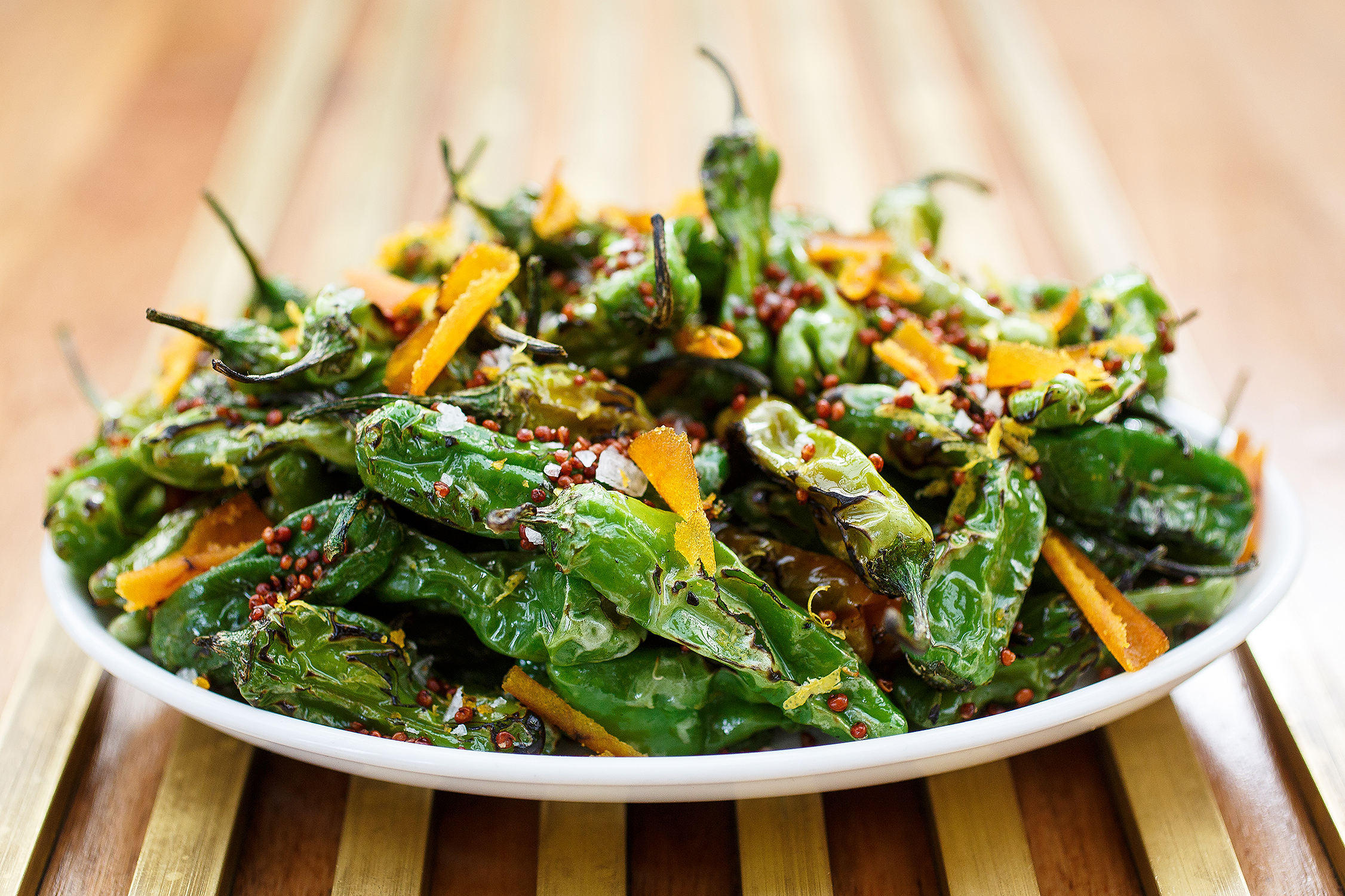 Plated vegetable dish featuring blistered green peppers and citrus garnish, photographed in natural light for editorial food photography.