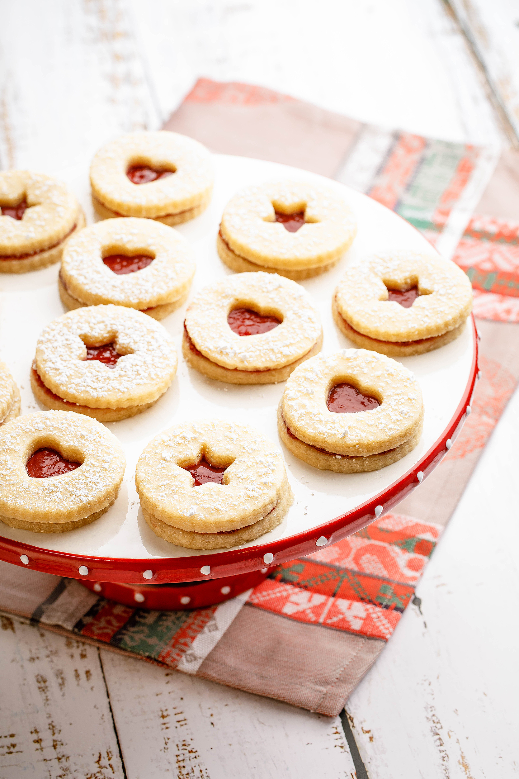 Vegan Linzer cookies with heart-shaped centers dusted with powdered sugar, photographed for a Christmas cookie cookbook.