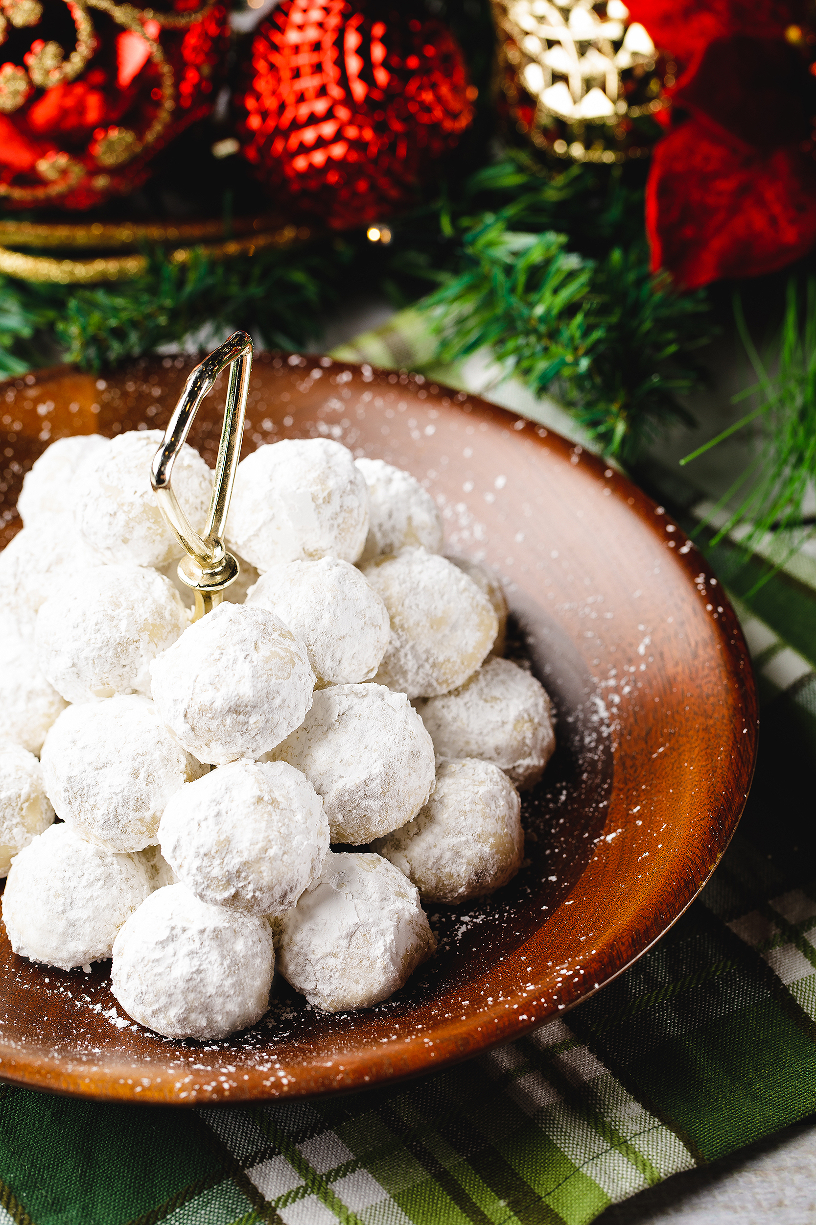 Vegan snowball cookies dusted with powdered sugar on a wooden plate surrounded by Christmas décor for a festive cookbook project.