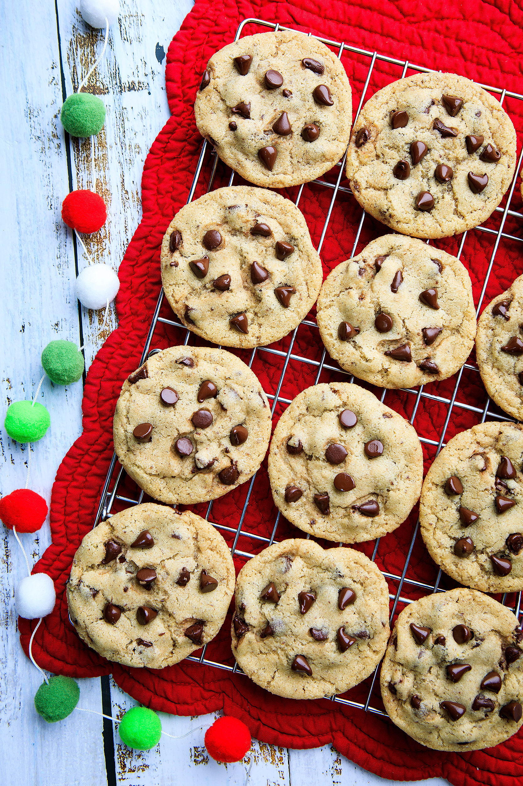 Vegan chocolate chip cookies cooling on a rack with festive Christmas decor, photographed for a holiday cookie cookbook by food photographer Vanessa Stump.