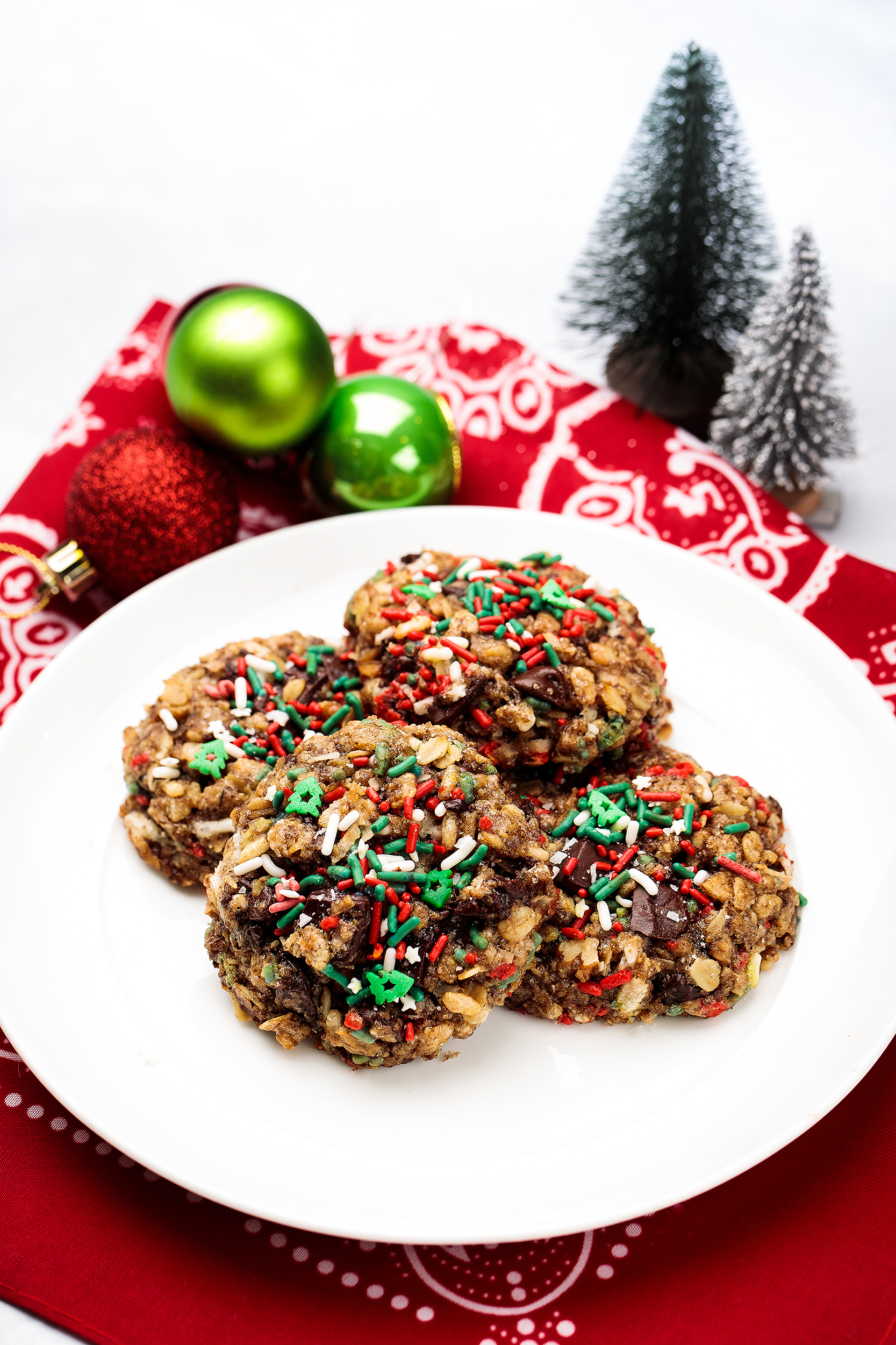 Vegan Christmas sprinkle cookies on a white plate with holiday ornaments, styled for festive cookbook photography.