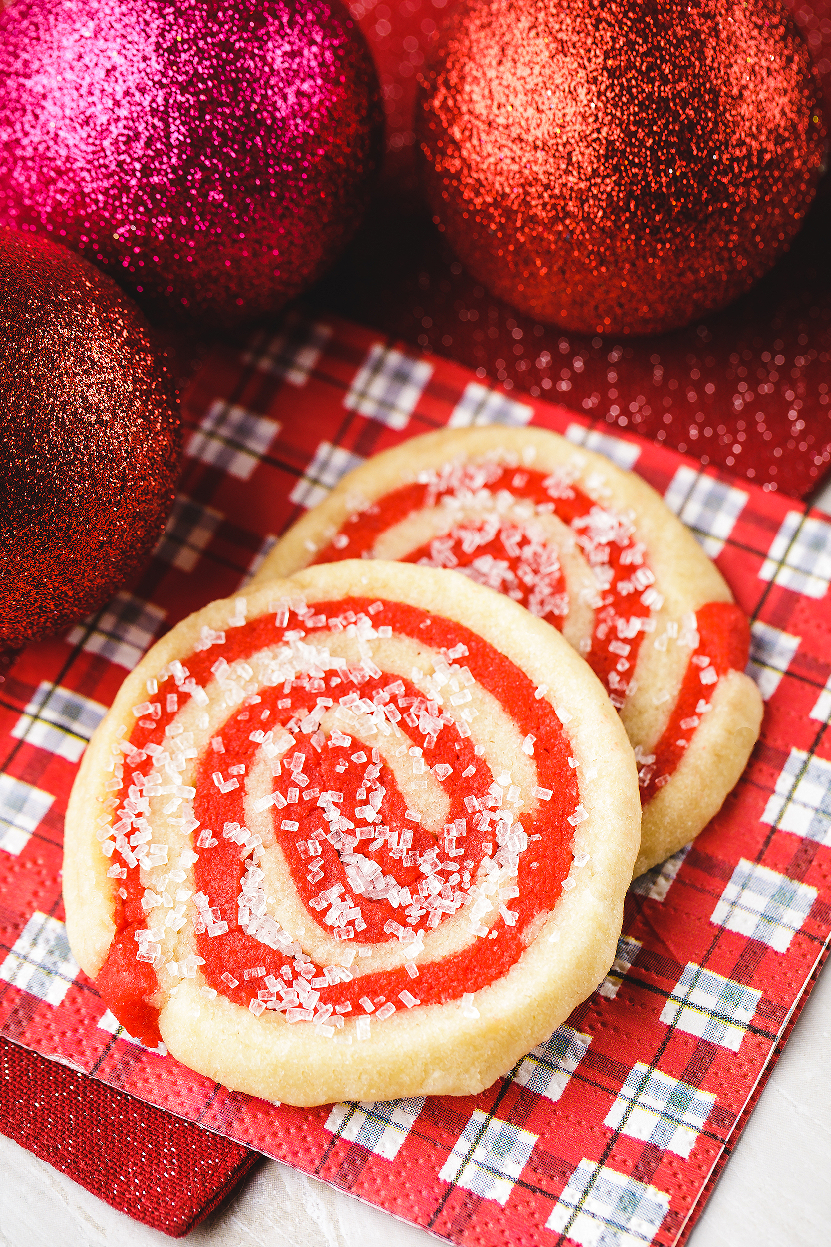 Vegan red and white Christmas swirl sugar cookies styled with glitter ornaments for a festive holiday cookbook photoshoot.
