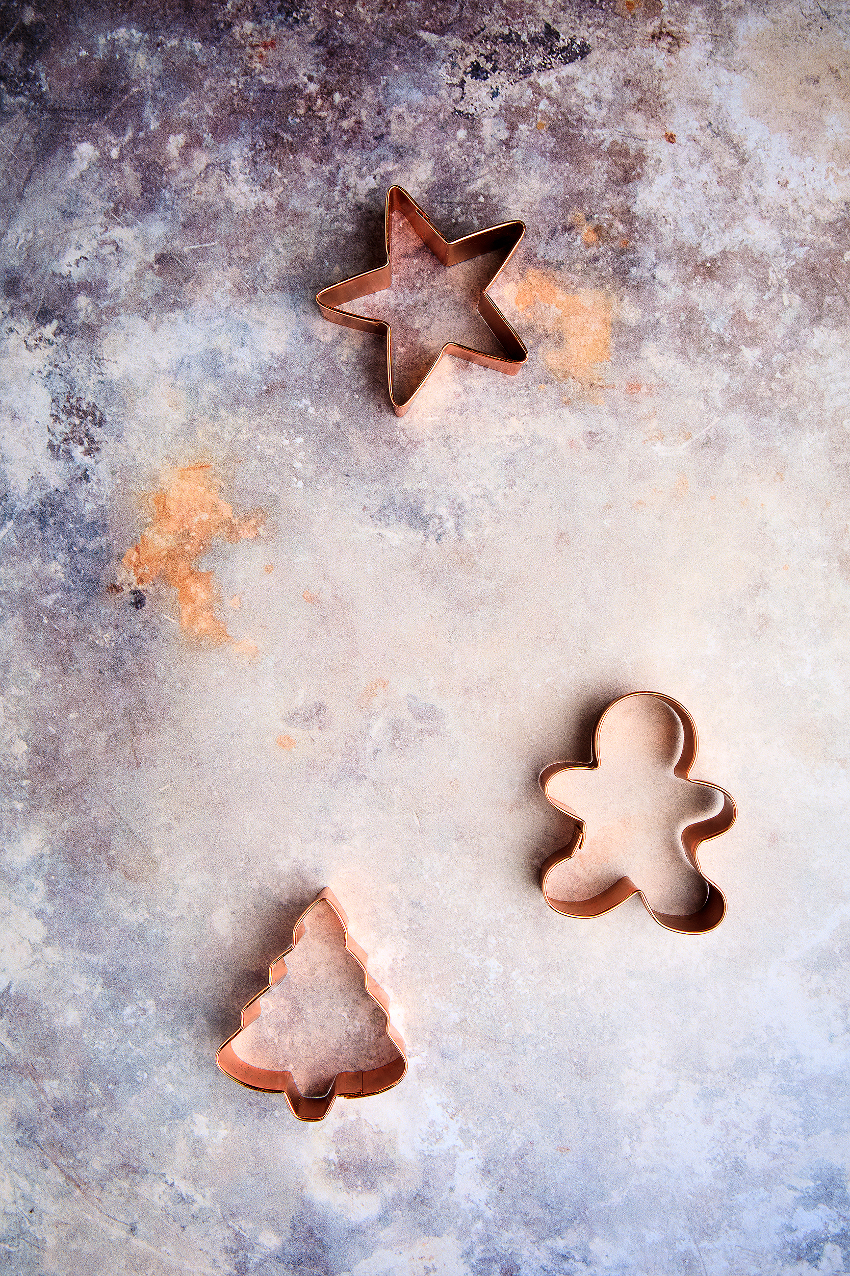 Holiday cookie cutters shaped like stars, gingerbread men, and trees on a rustic baking surface for a vegan Christmas cookbook photoshoot.
