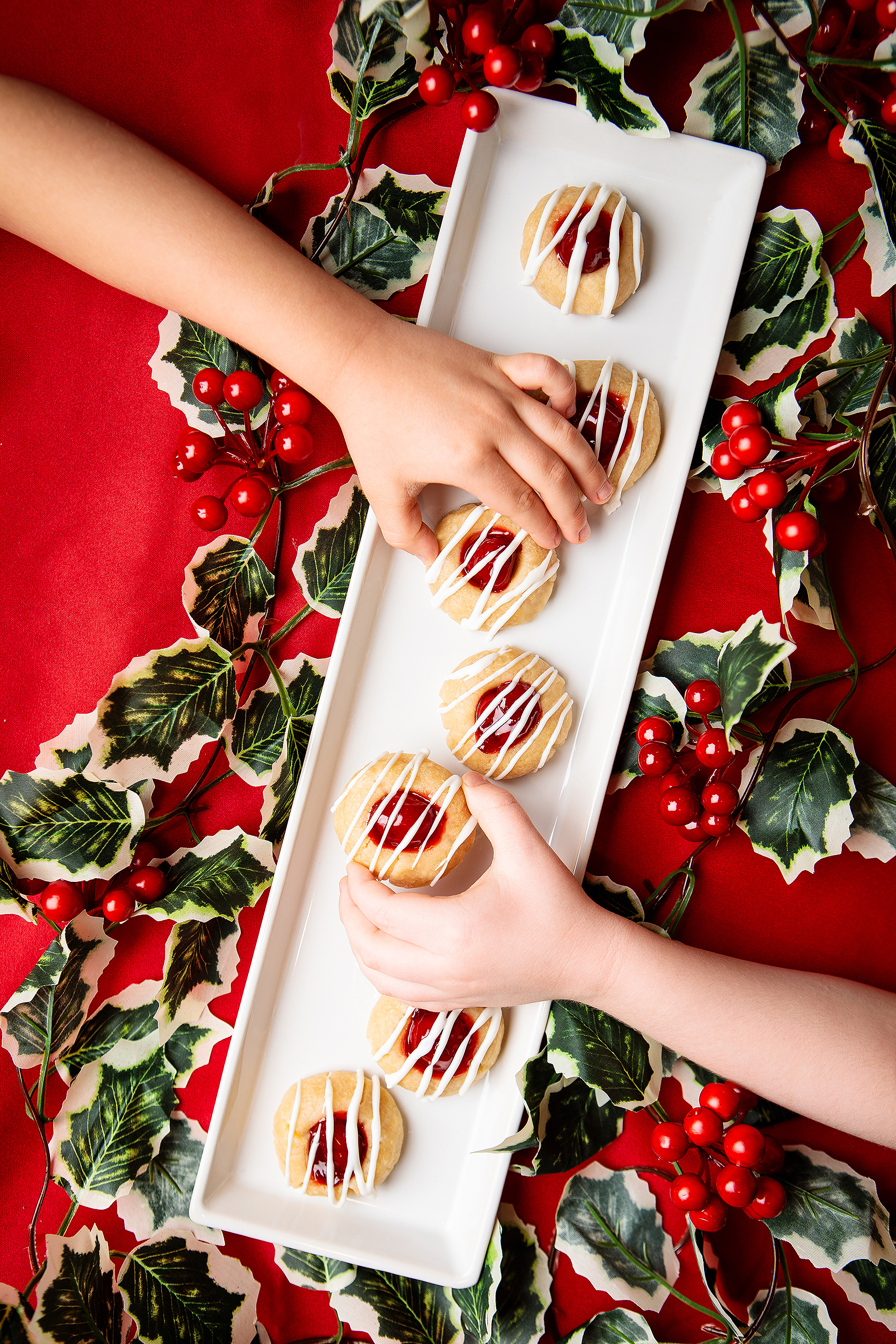 Kids hands reaching for vegan Christmas cookies with icing on a festive red holiday backdrop, photographed for a vegan cookie cookbook.