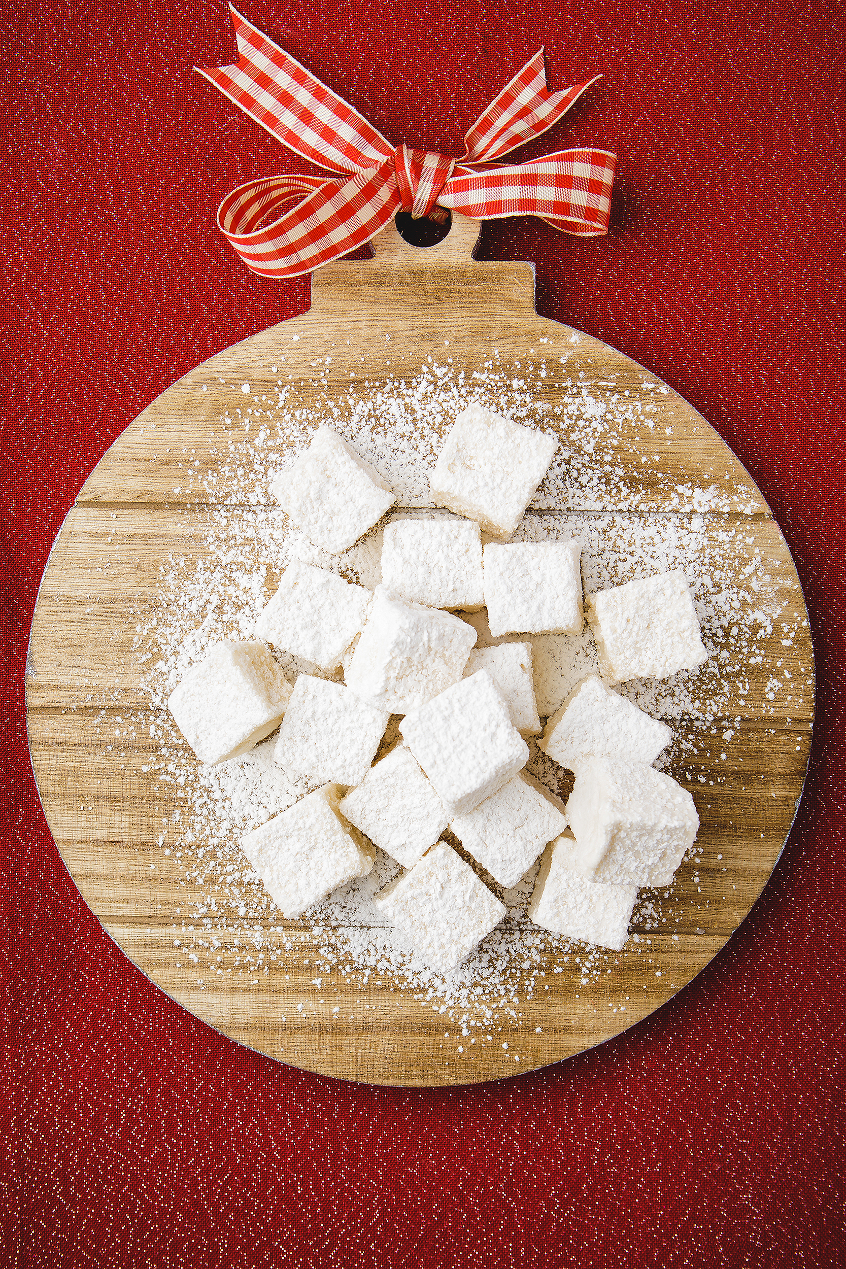 Vegan homemade marshmallows styled on a wooden ornament board and dusted with powdered sugar for a holiday cookbook photoshoot.