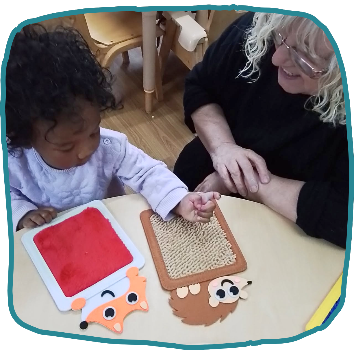 A child and an older woman explore textured animal-shaped boards on a table in nursery at Morden