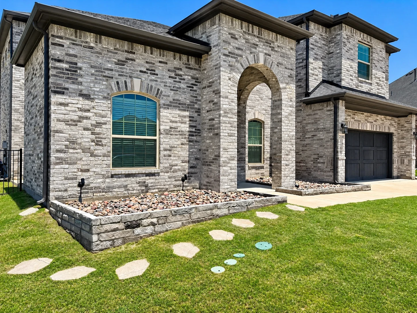 Hand-laid stone edging with layered evergreen shrubs and fresh dark mulch for a clean, intentional bed.