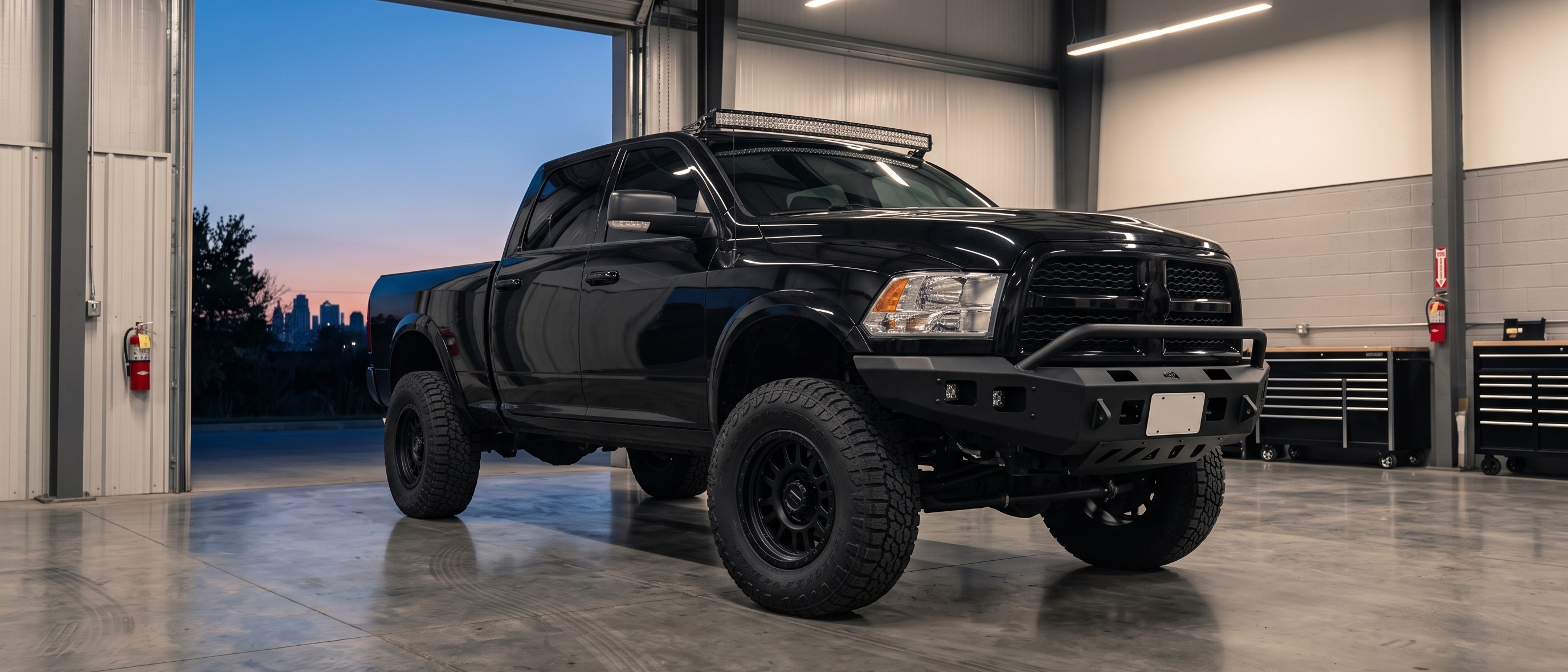 A lifted black pickup truck with aftermarket wheels and a light bar, finished and parked in a shop bay