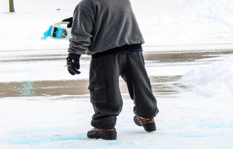 Snow removal near me homeowner spreading blue ice melt on an icy driveway