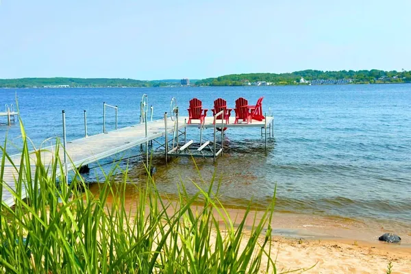 Dock with four red Muskoka chairs over clear Georgian Bay water at Bayside in Midland