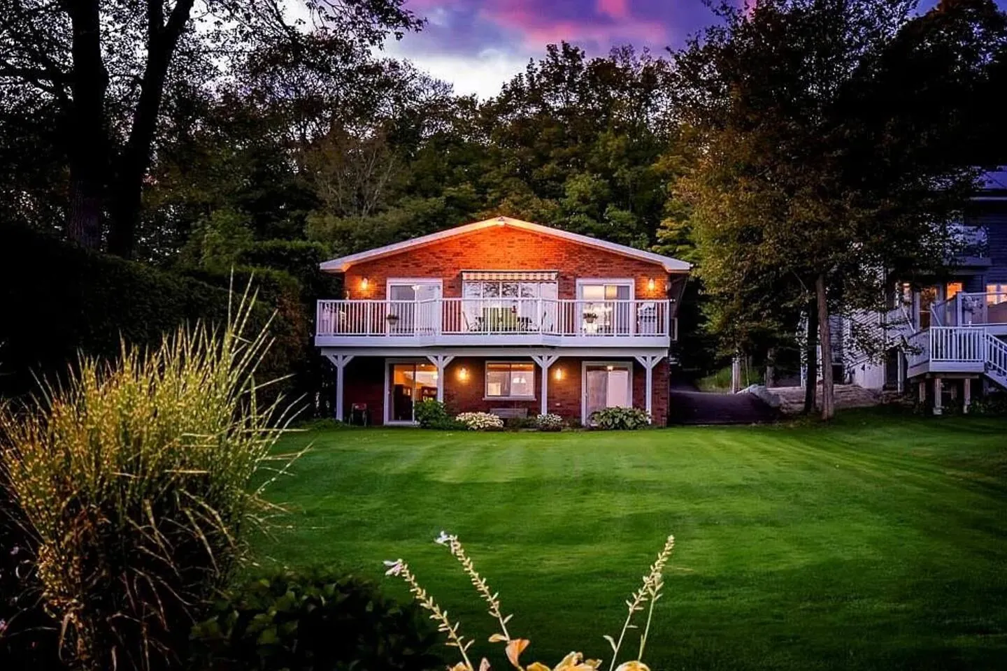Bayside cottage lit at dusk above a striped lawn