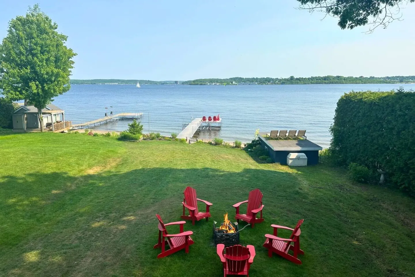 Red Muskoka chairs around a fire pit on the Bayside lawn with the bay beyond