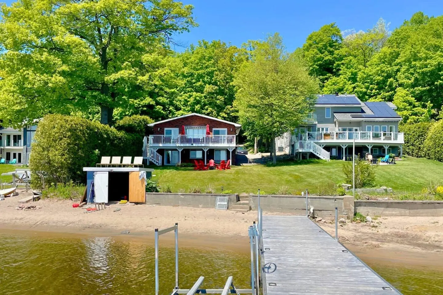 Bayside seen from the water: sand beach, boathouse, dock and the cottage on the lawn