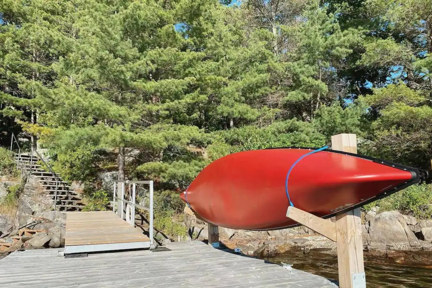 Red canoe on a rack beside the Hemlock Hideaway dock, with pine trees and rock