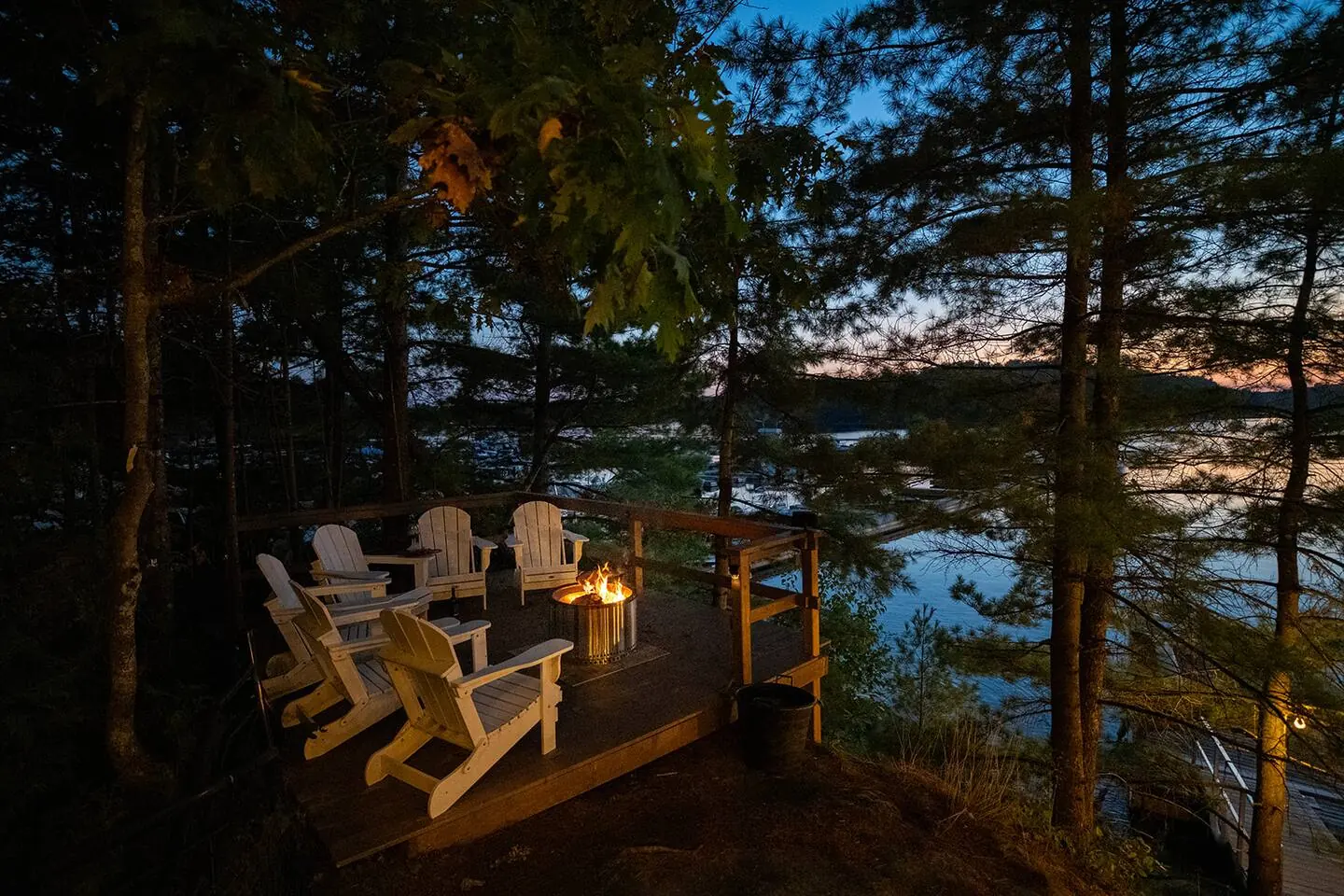 Muskoka chairs around a fire pit on the rock by the water at Hemlock Hideaway at dusk