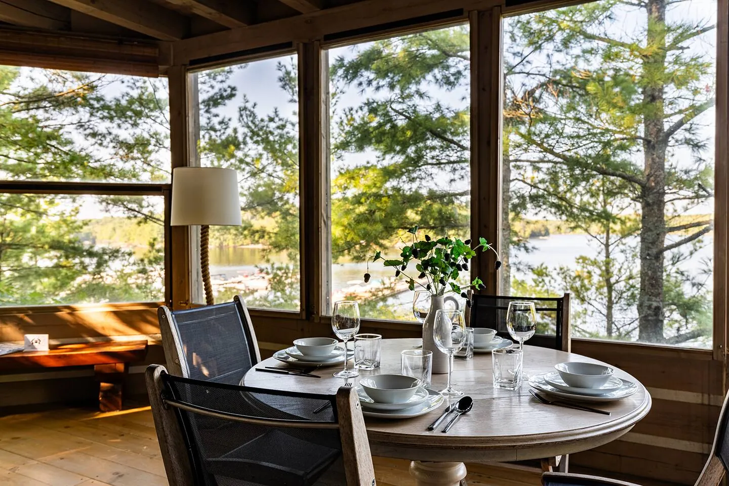 Screened Muskoka room at Hemlock Hideaway with a round table set for dinner and pine trees beyond