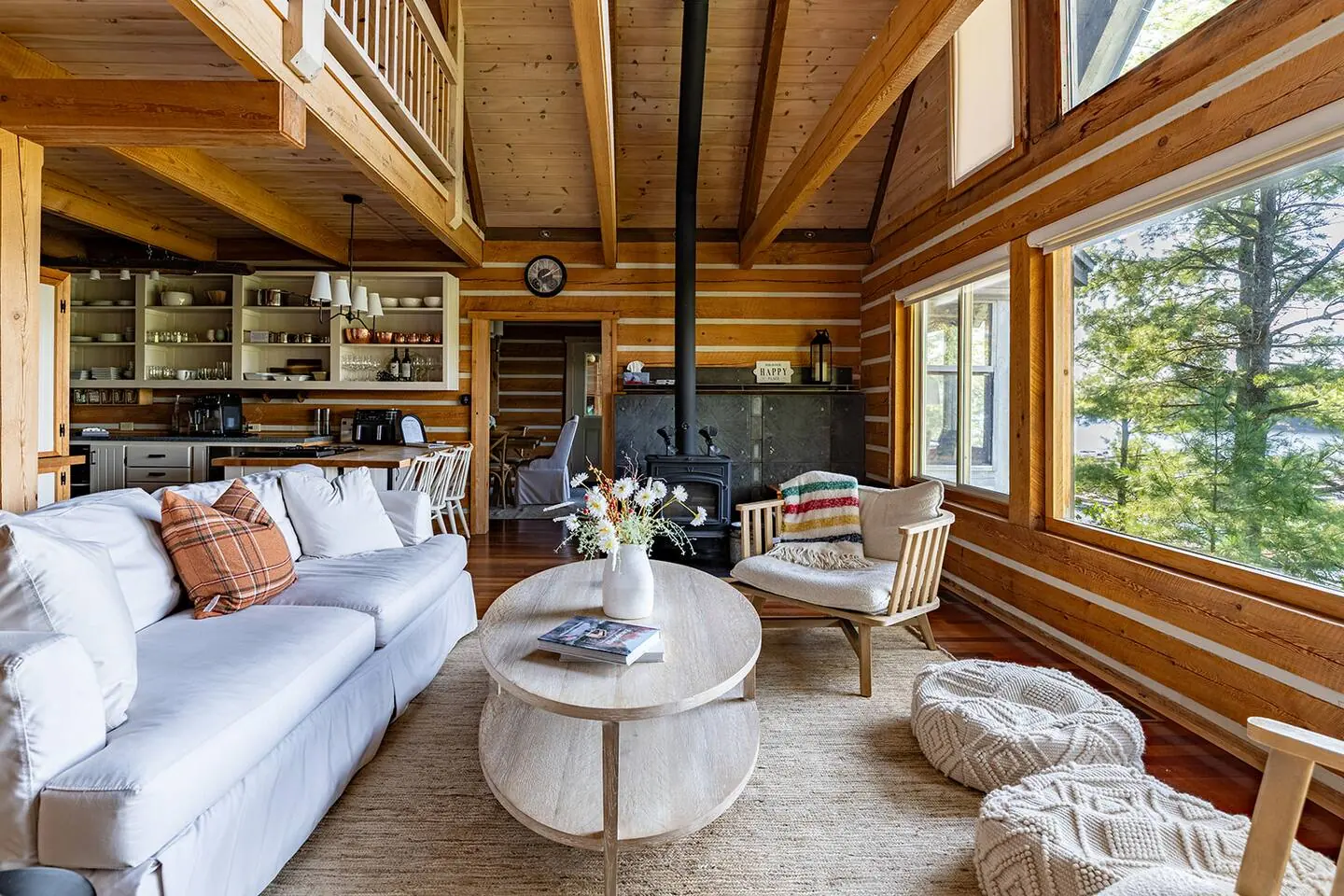 Log-walled living room at Hemlock Hideaway with white sofas, a wood ceiling and tall windows to the trees