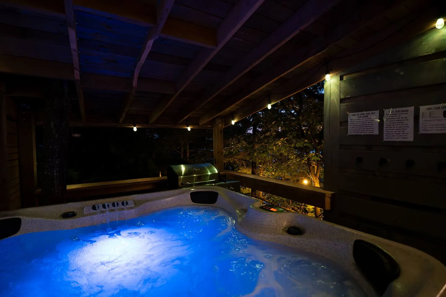 Hot tub glowing blue at night under the covered patio at Hemlock Hideaway
