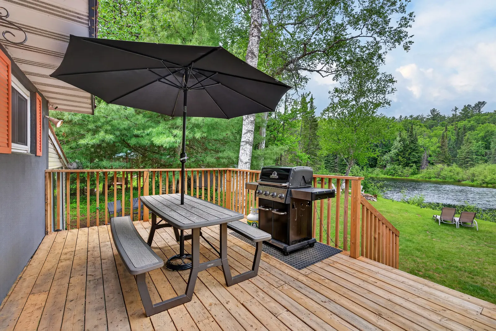 Deck at The Mara with a barbecue and an umbrella table looking down to the river
