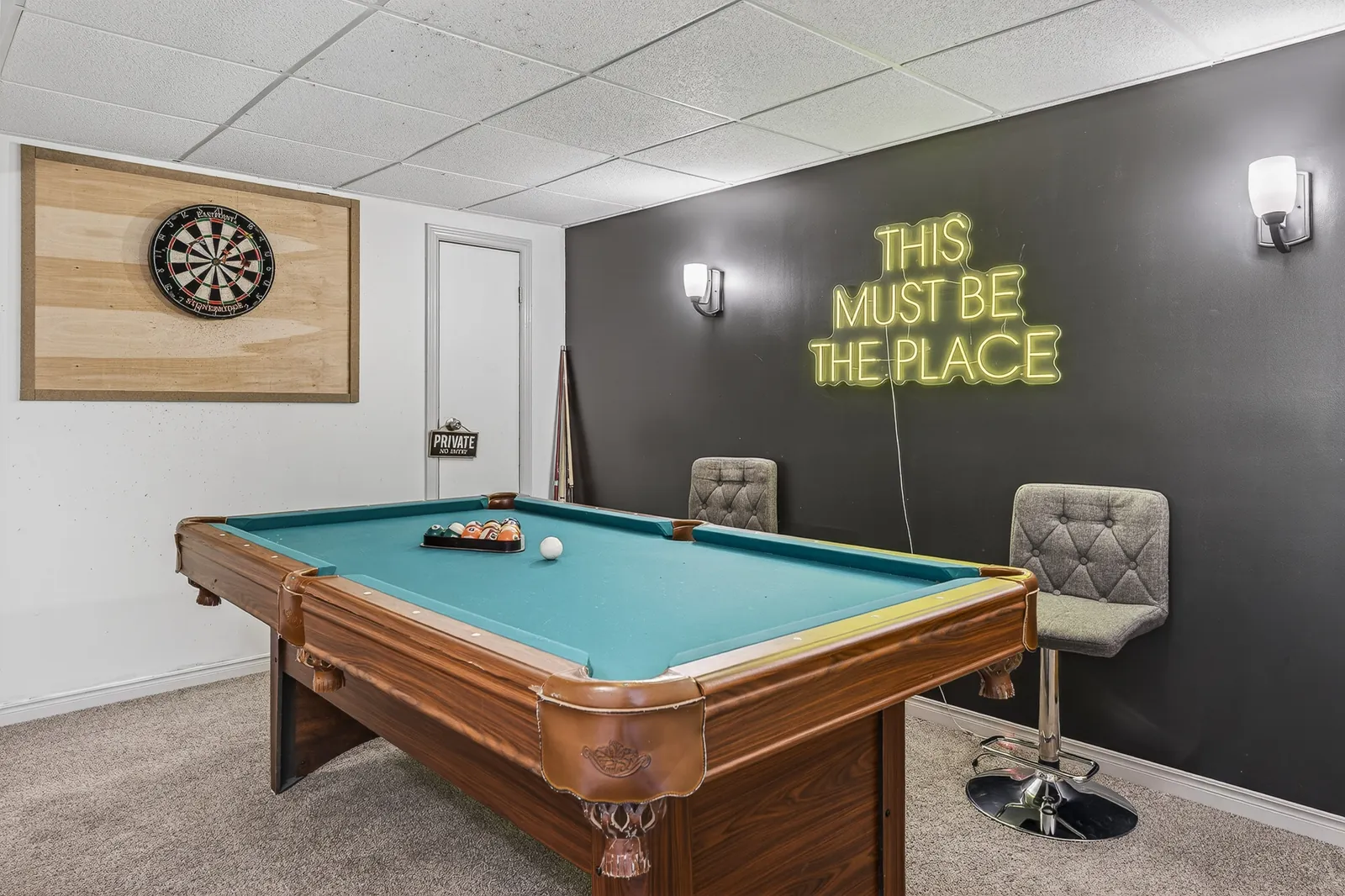 Lower-level game room at The Mara with a pool table, dartboard and a neon sign