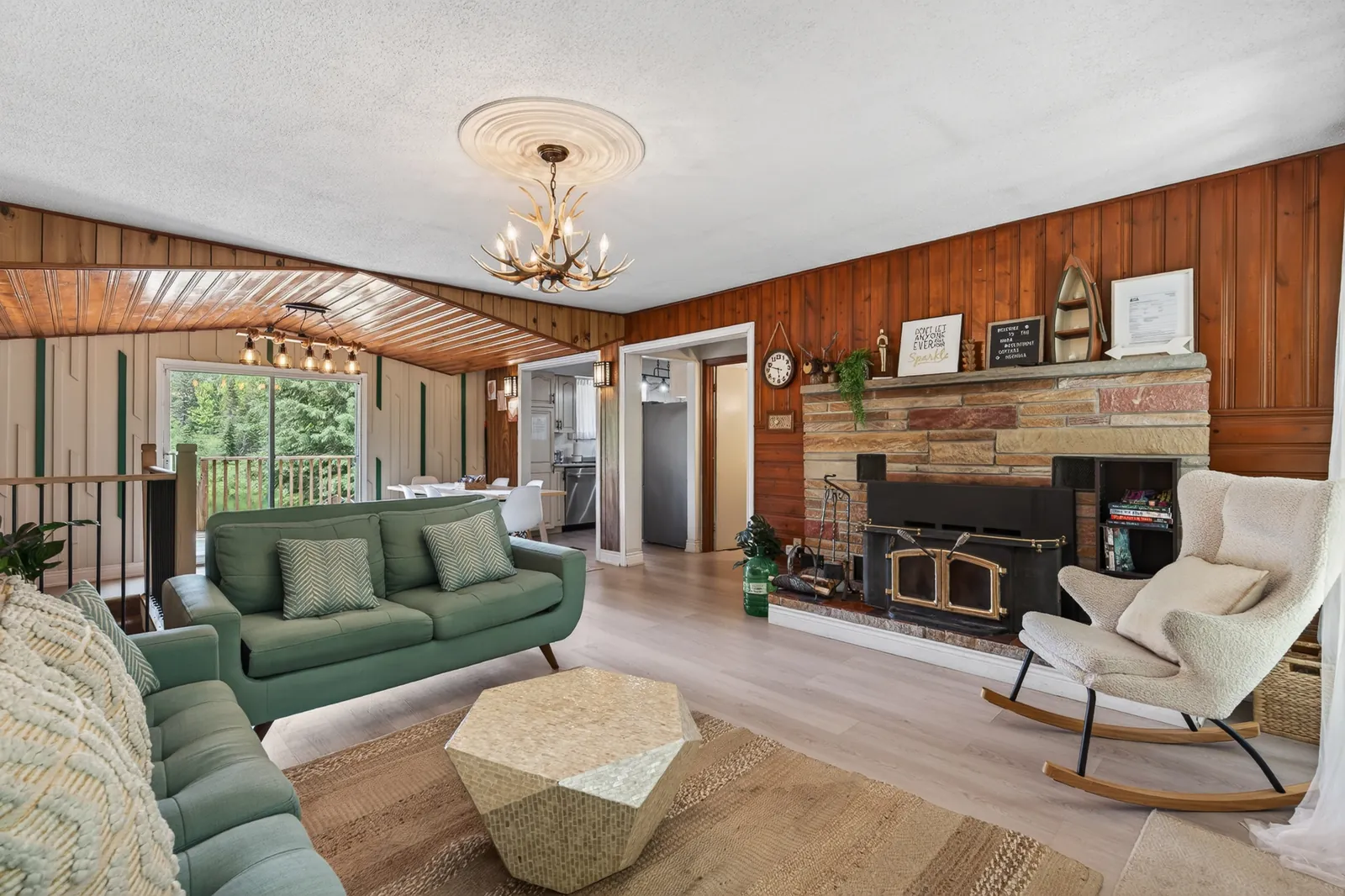 Wood-panelled living room at The Mara with a stone fireplace, green sofas and a rocking chair