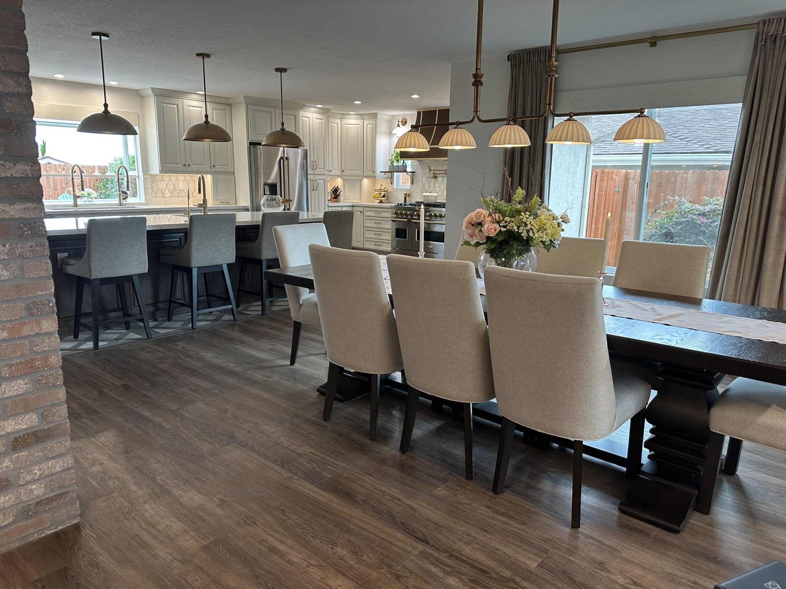 Open dining area flowing into the new kitchen with linen chairs, long wood table and brass linear chandelier