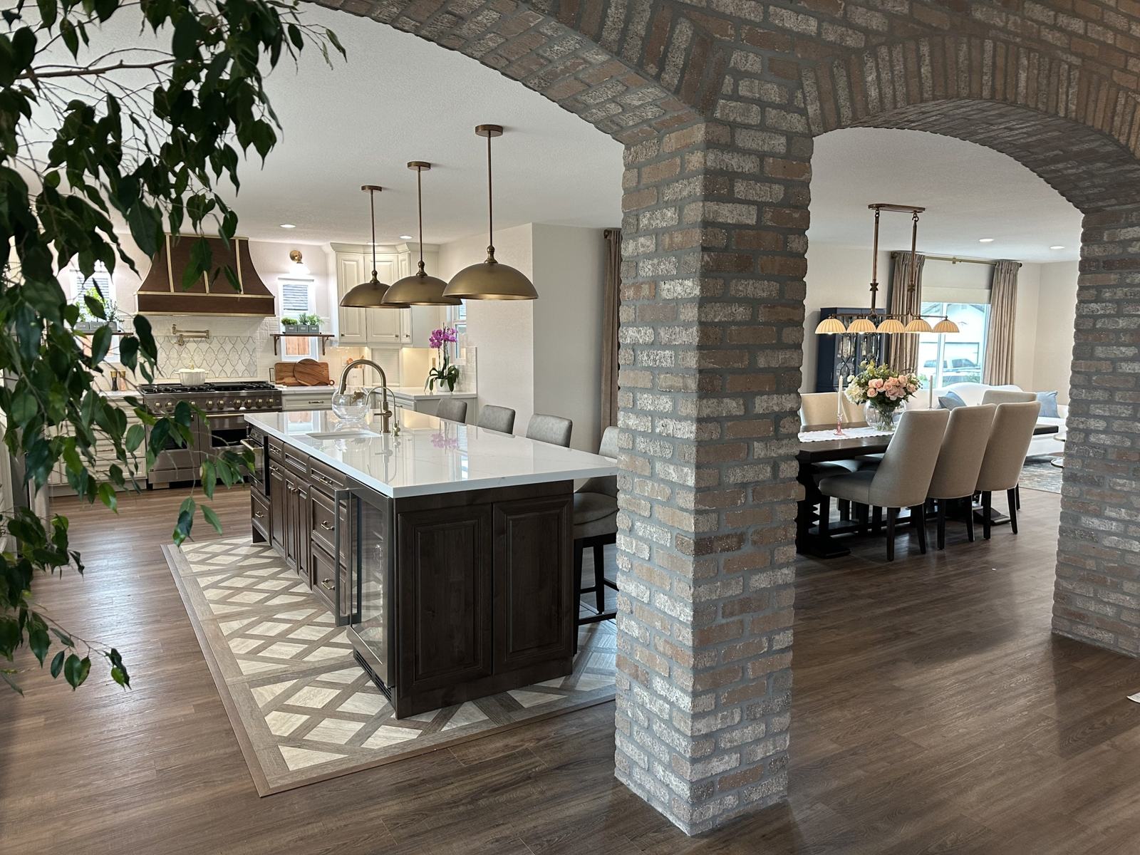 Finished kitchen framed by two brick archways with island, range hood and dining area