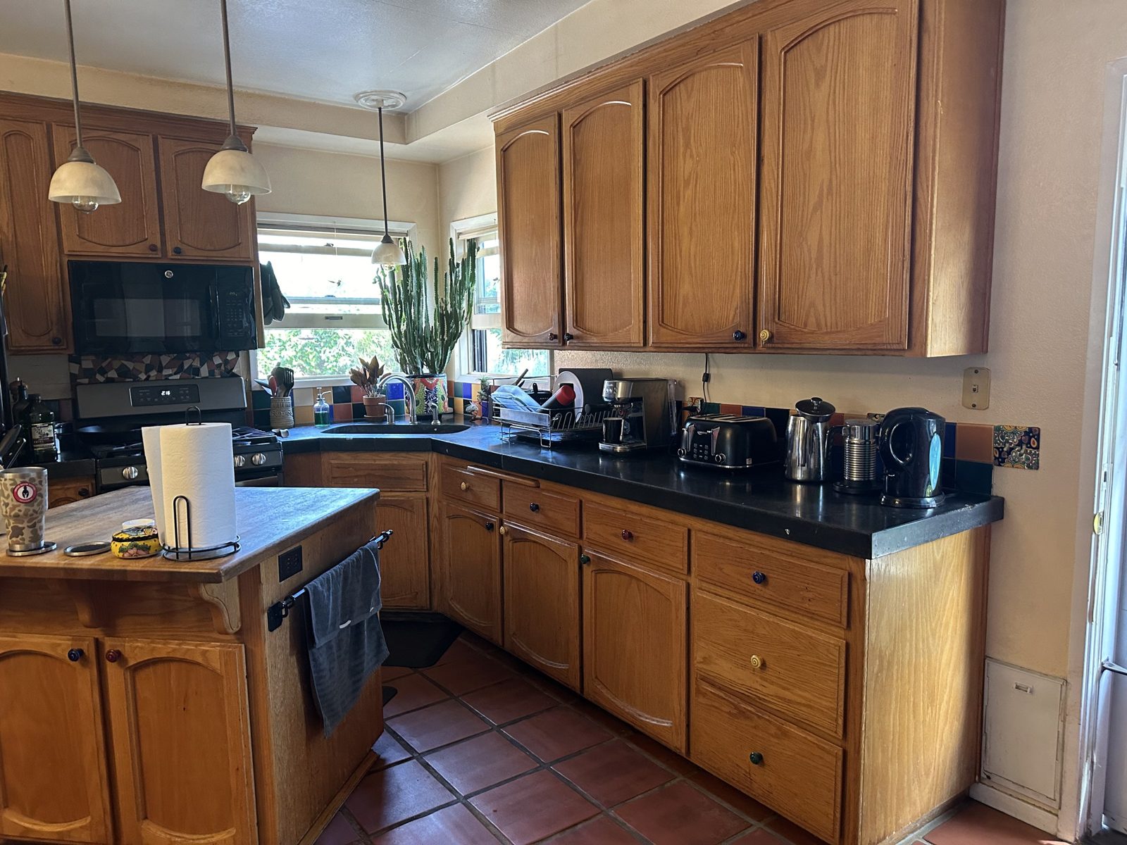 Oak kitchen cabinets with black countertops and colorful tile backsplash before remodel