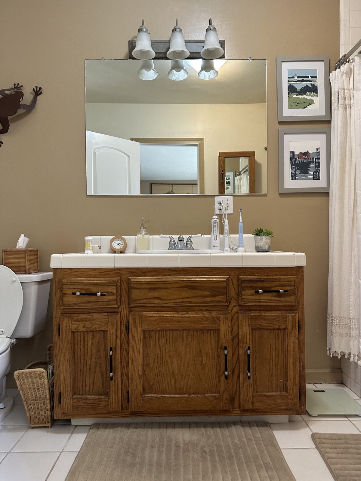 Bathroom before remodel with single oak vanity, tile countertop and beige walls
