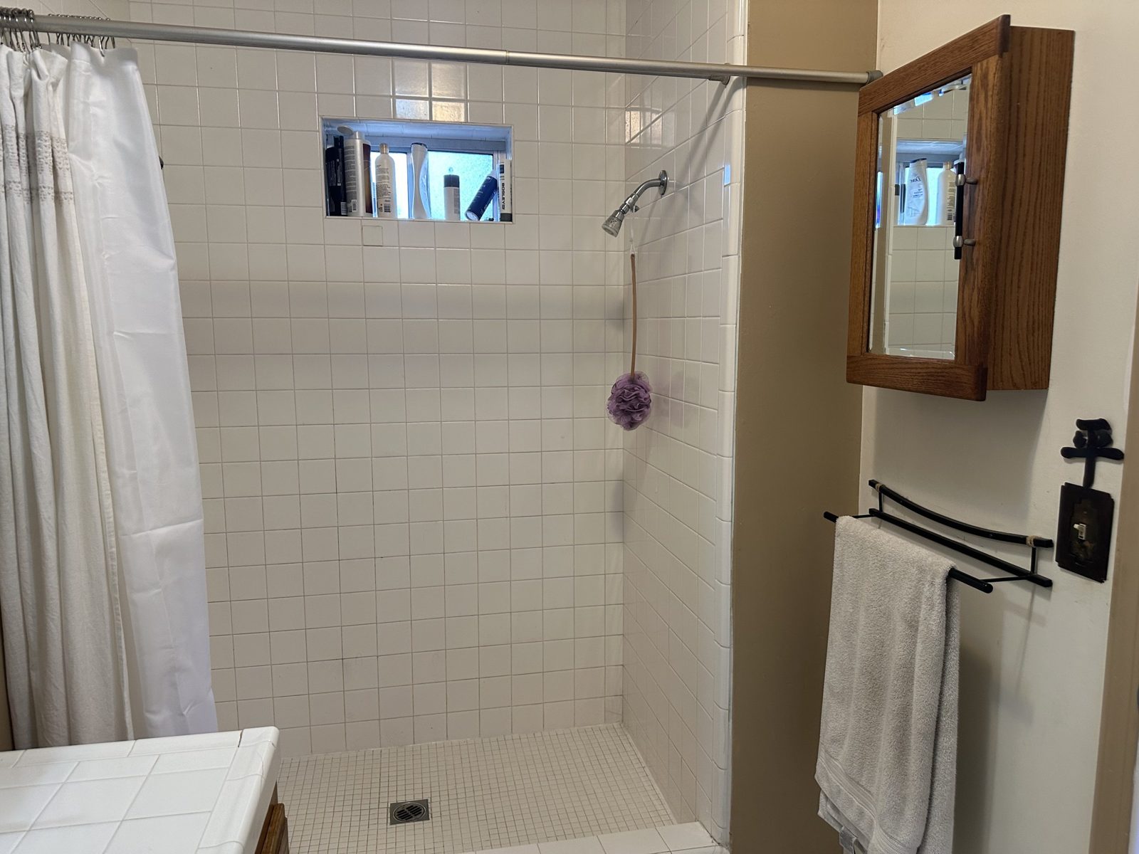 Shower before remodel with white square tile and shower curtain