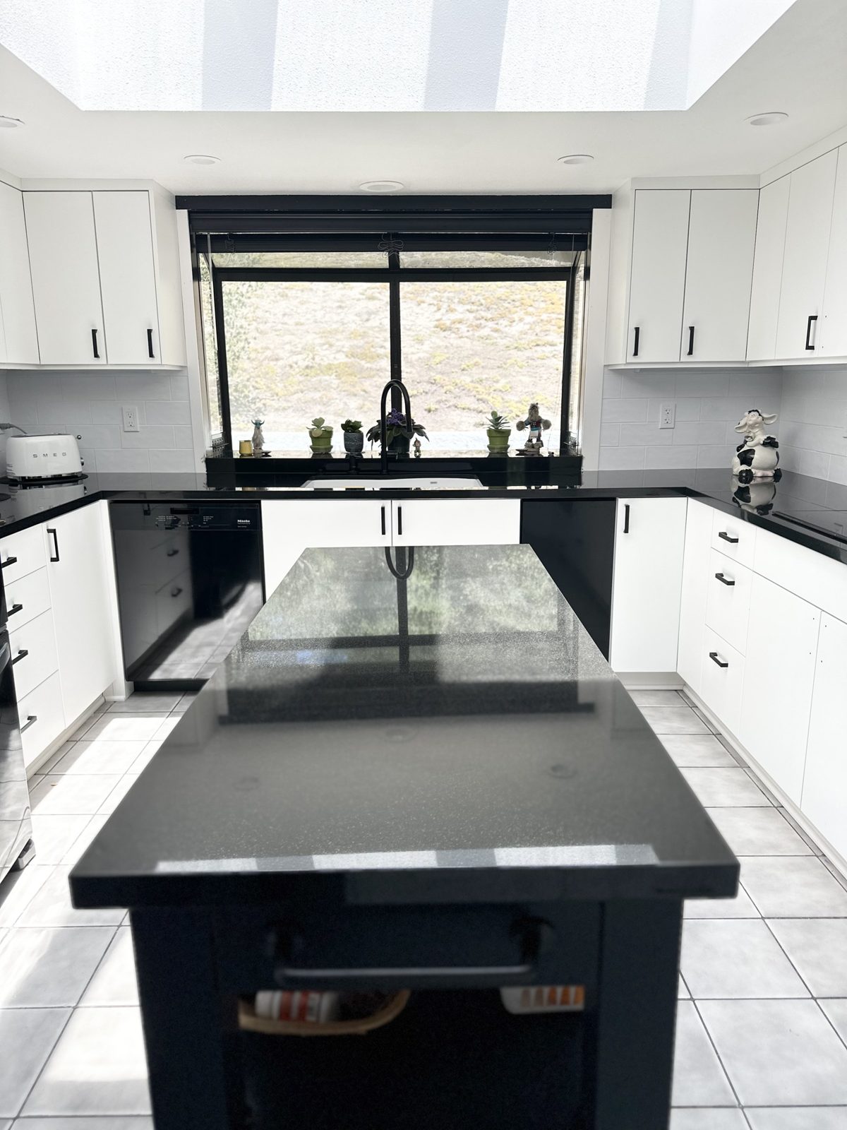 Modern white kitchen with black countertops, black island and skylight
