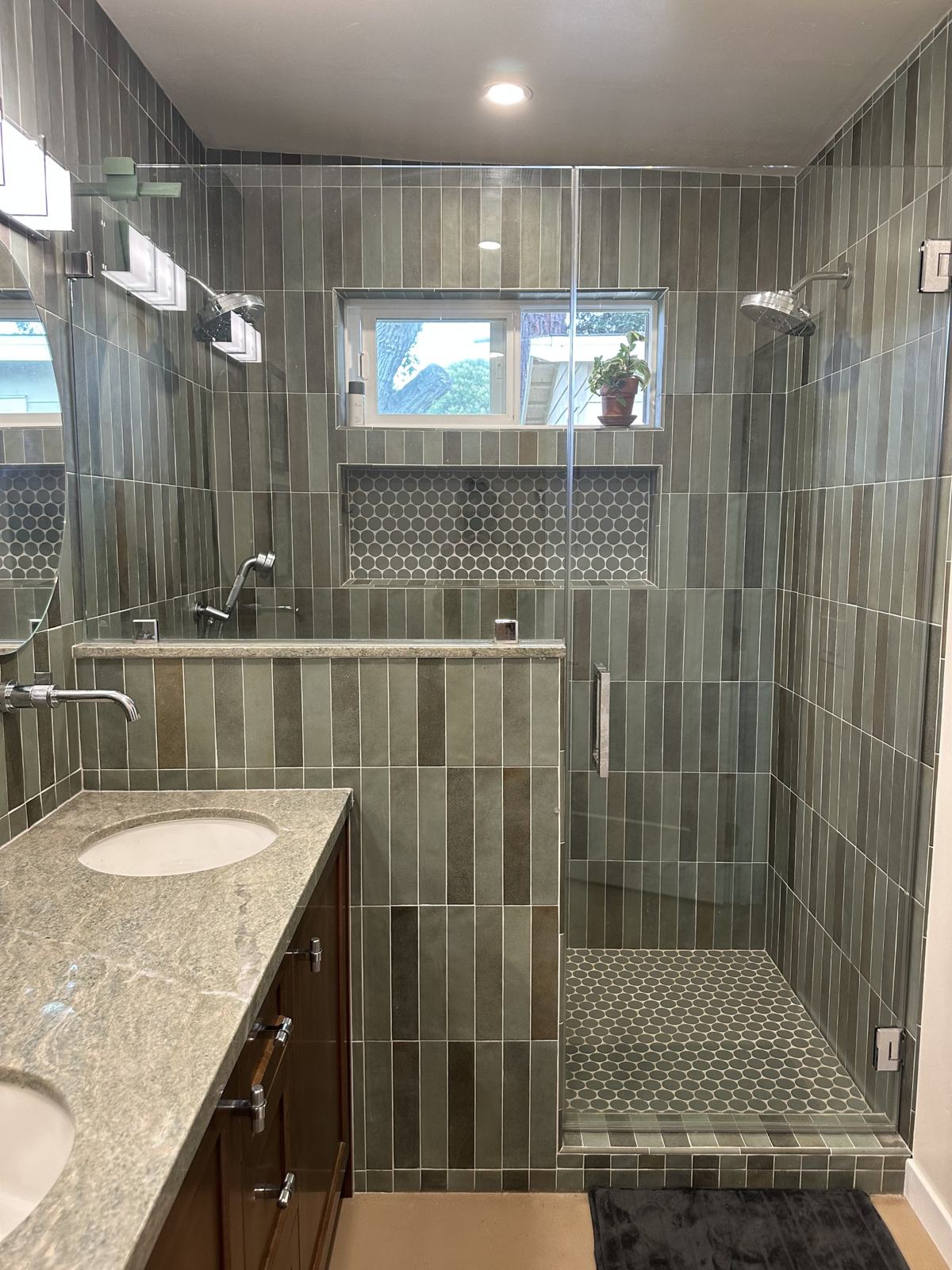 Frameless glass walk-in shower with green tile, hexagon tile niche and window