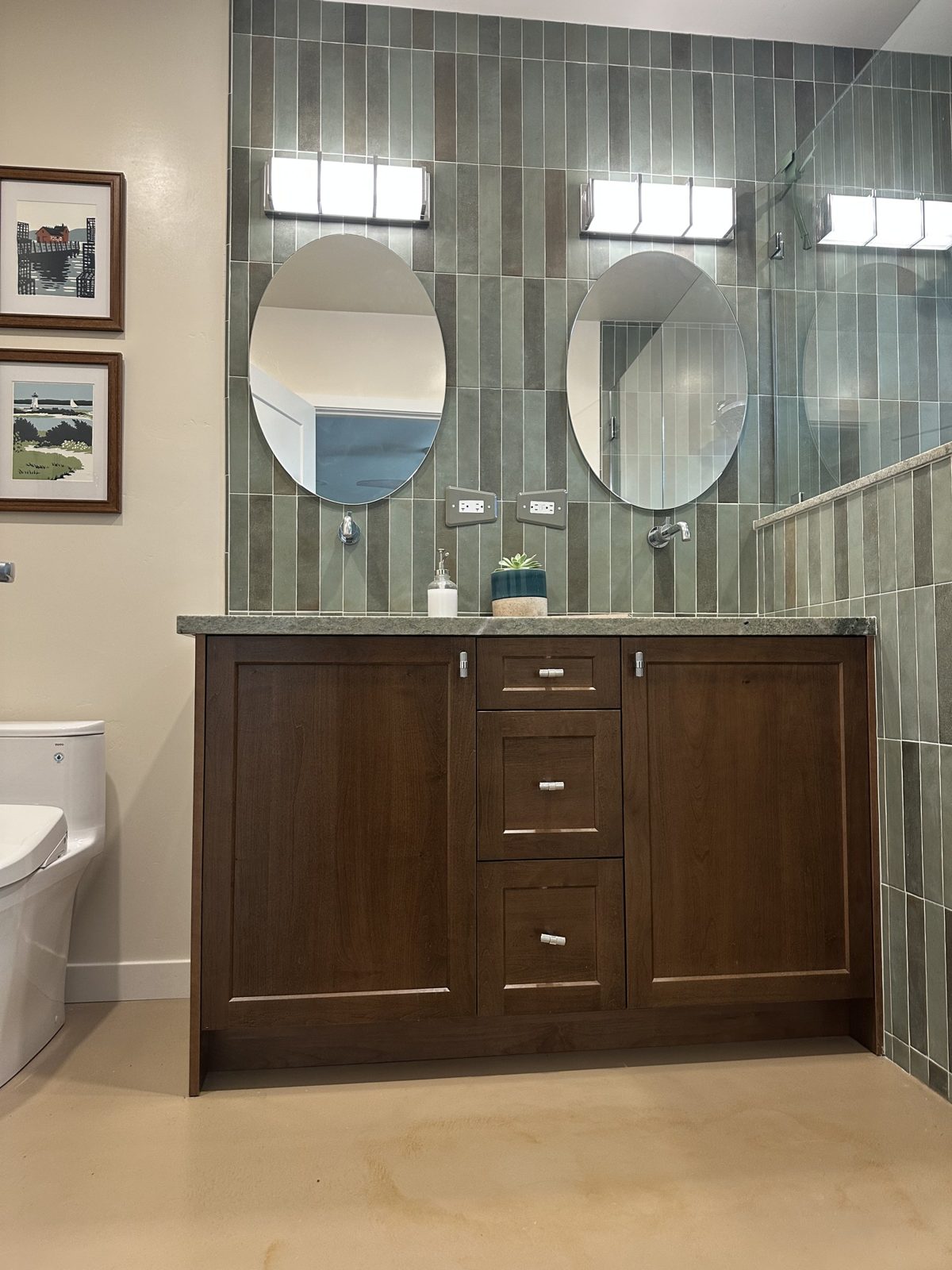 Remodeled bathroom with double walnut vanity, oval mirrors and vertical green stacked tile
