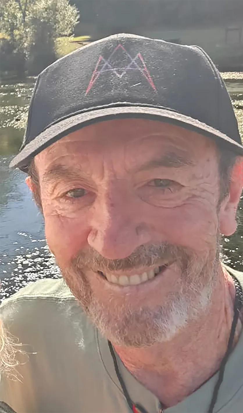 Jonathan Quintin smiling by a river, wearing a black cap with a geometric emblem
