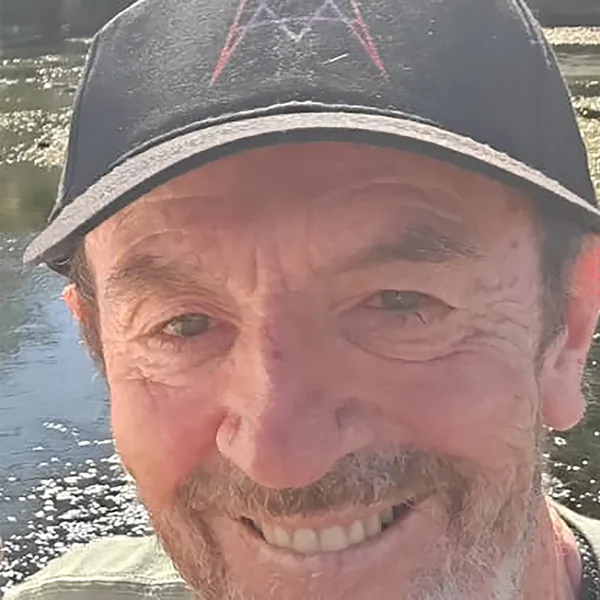 Portrait of Jonathan Quintin by a river, wearing a black cap
