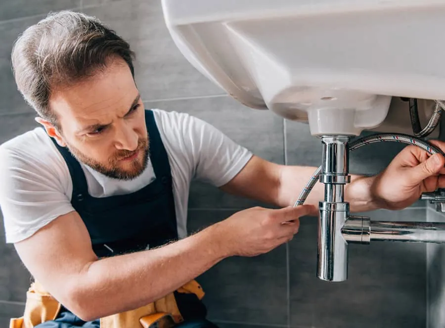 Plumber repairing the drain fittings under a bathroom sink