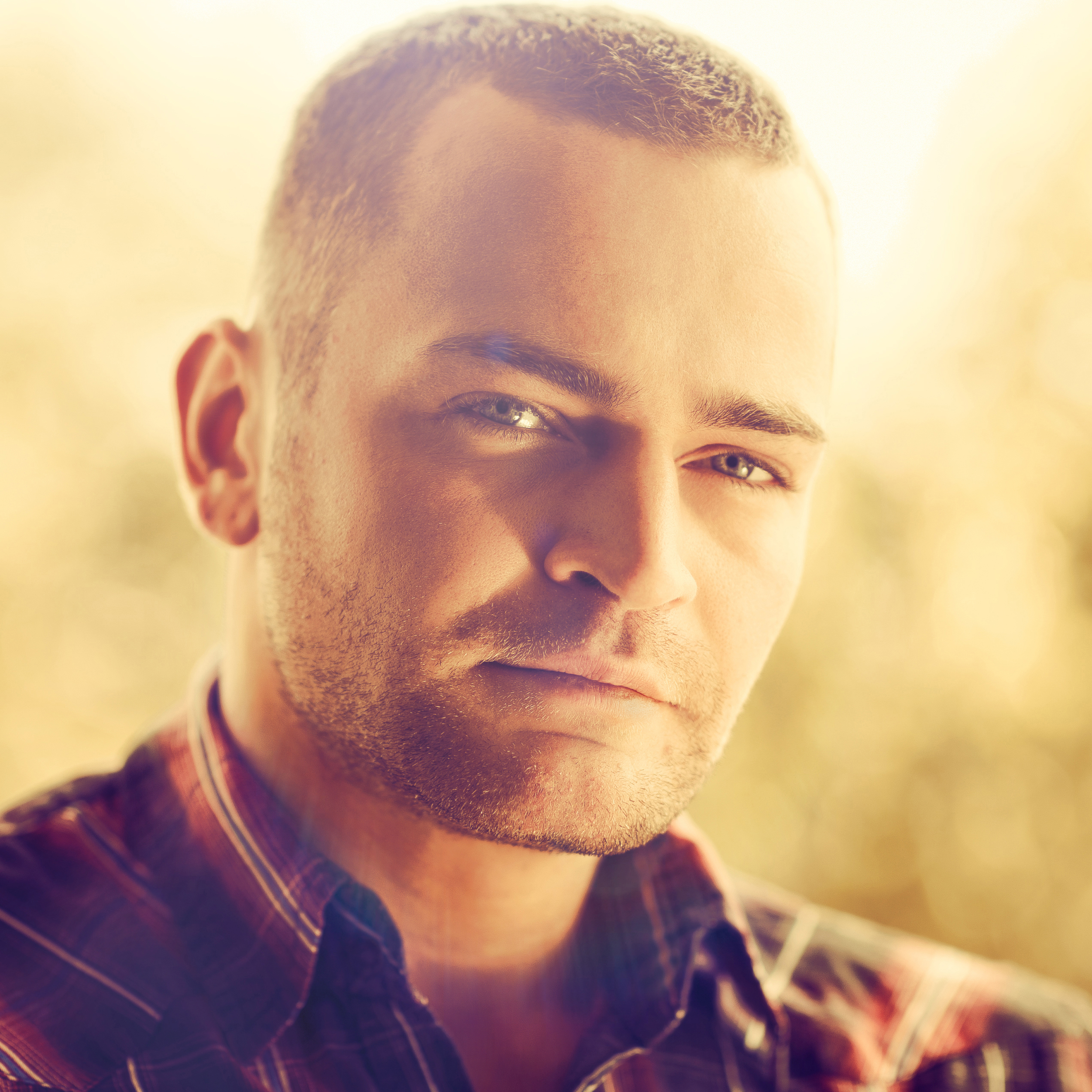 Man with short hair and a serious expression, wearing a plaid shirt, illuminated by soft natural light, reflecting confidence and wellness, relevant to testimonials about effective treatments at My Ageless Lounge.