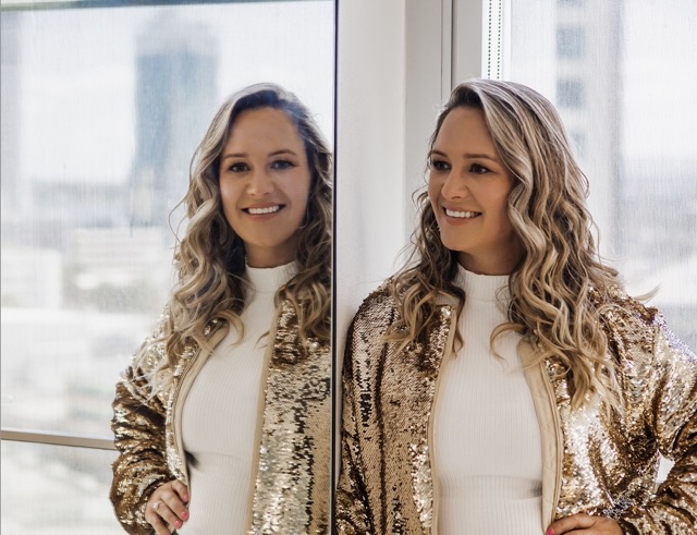 Fleur Lonsdale beside a mirror in a gold sequin jacket, city skyline behind her