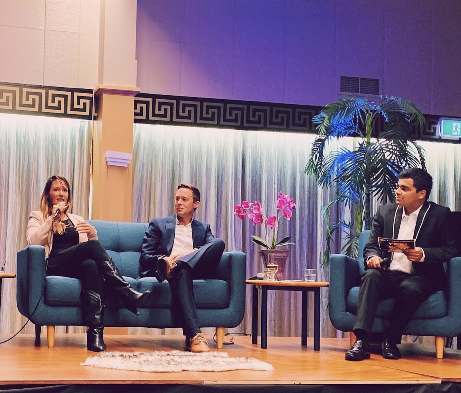 Fleur Lonsdale speaking with a microphone on a panel of three, on stage at a live event