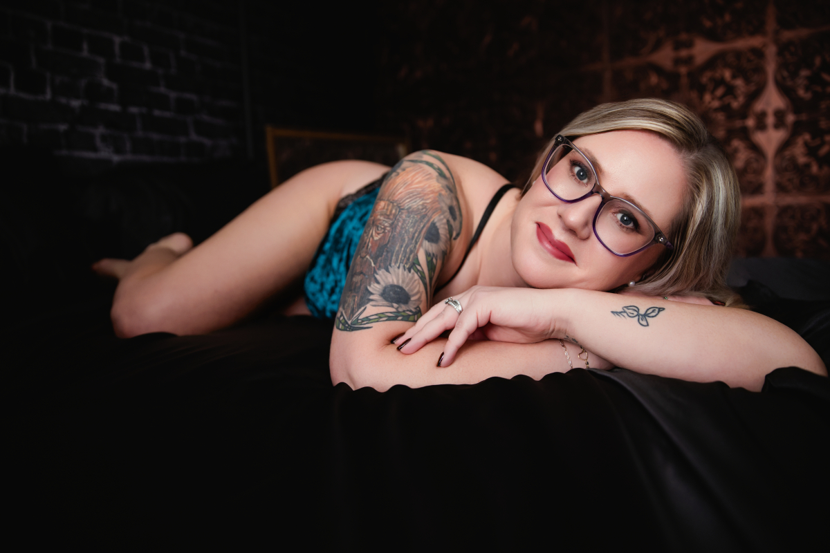 A blonde woman with glasses poses in turquoise lingerie for a boudoir shoot in Indianapolis at Enchanted Moments Artistry.