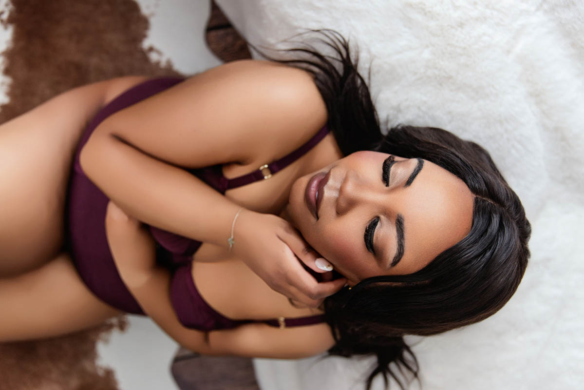 A woman in maroon lingerie poses on a bed for a boudoir shoot in Indianapolis at Enchanted Moments Artistry.