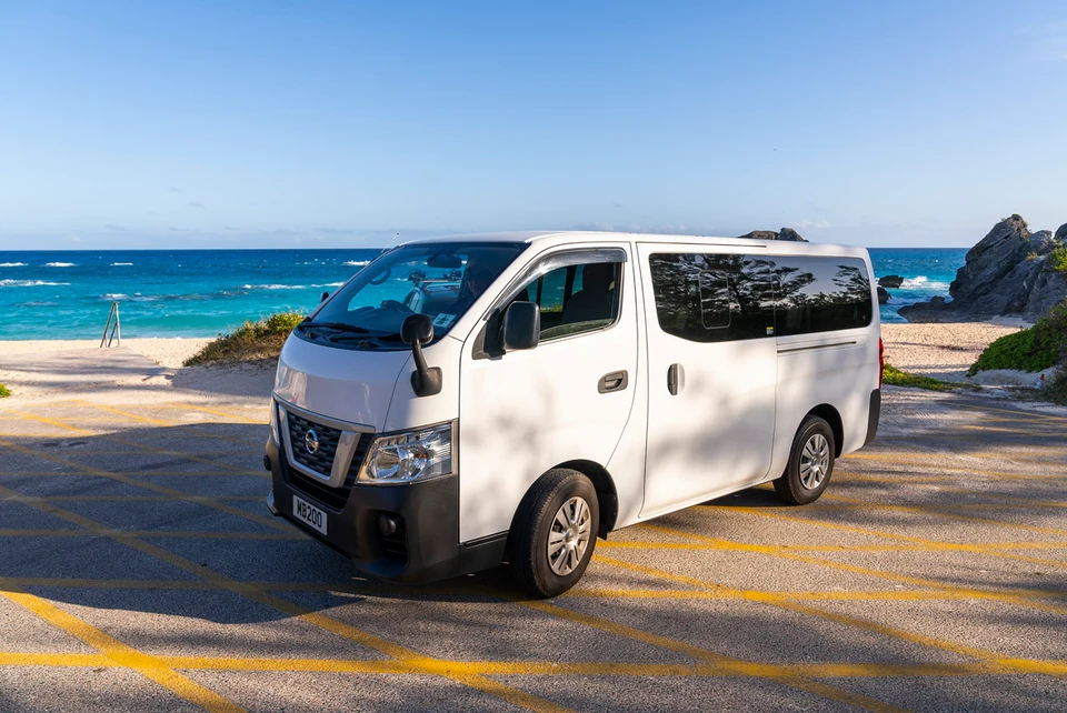 The white INTO Bermuda Nissan minibus parked beside a turquoise Bermuda beach