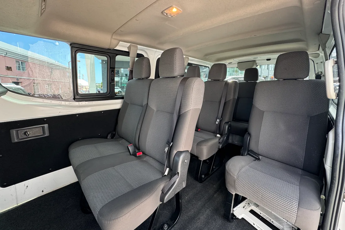 Three rows of grey passenger seats inside the minibus, seen from the side door