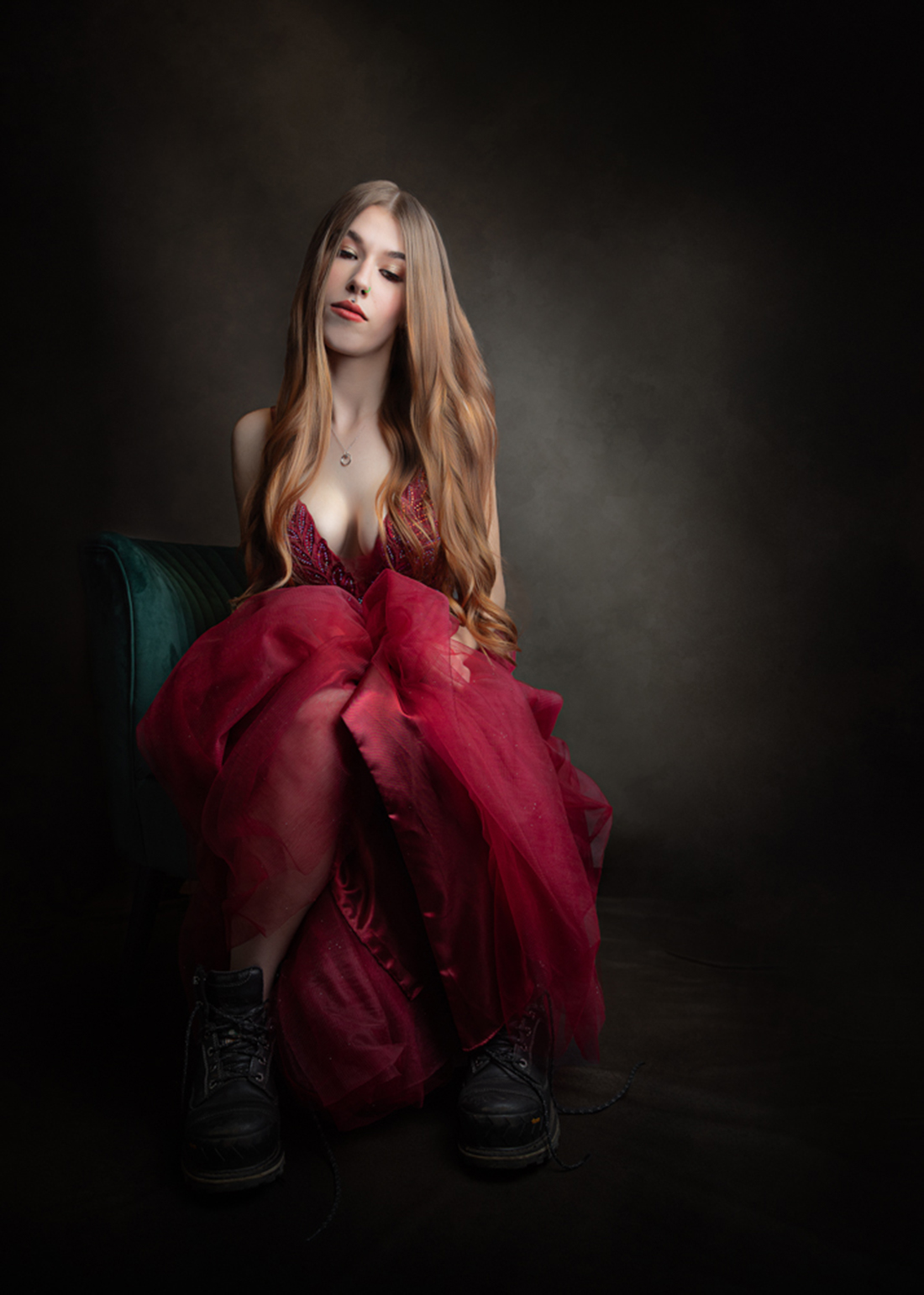 Editorial-style portrait of a young woman in a flowing red dress seated in dramatic studio lighting by Janice Smith Photography in Surrey BC