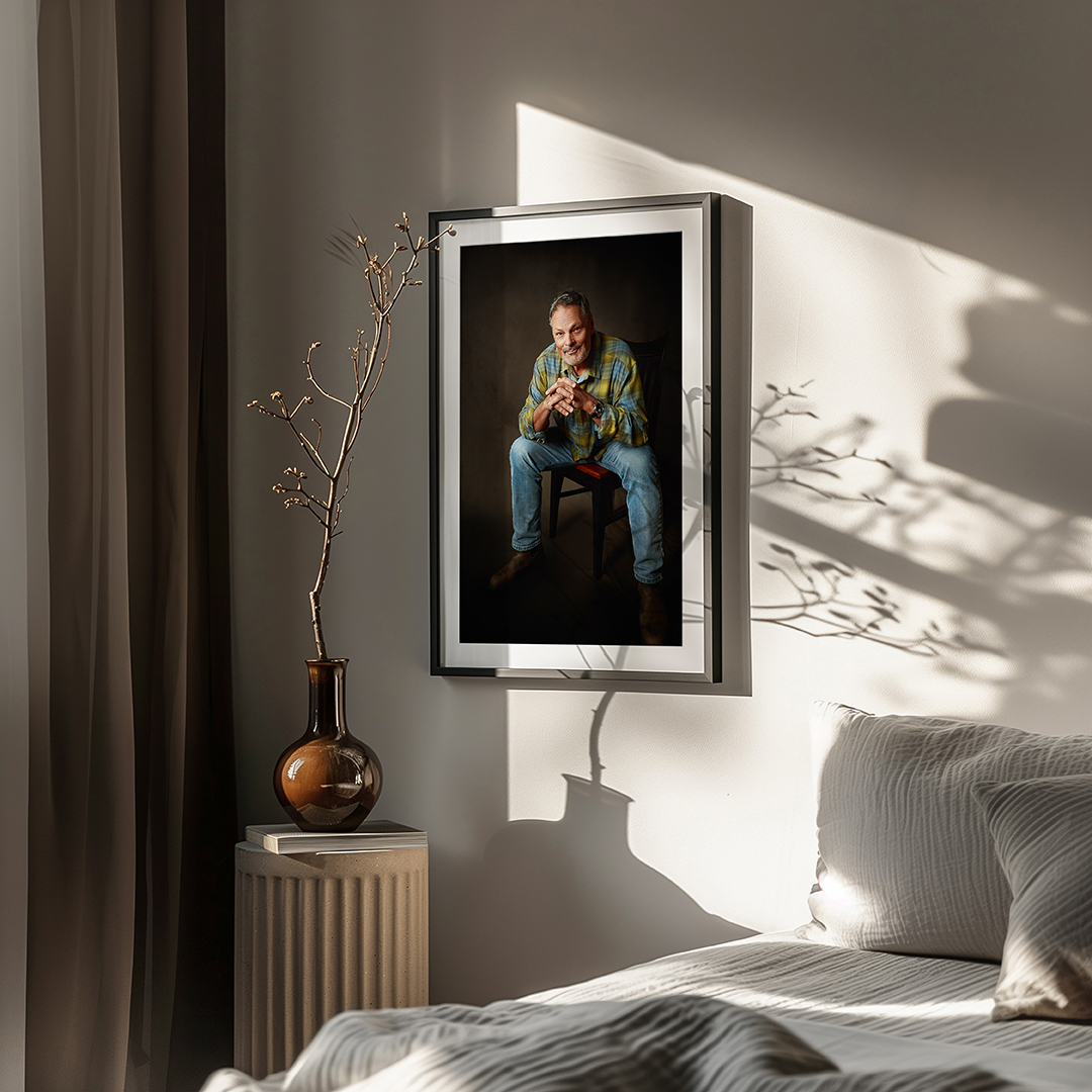 Framed fine art portrait of a man displayed as wall art in a softly lit bedroom.