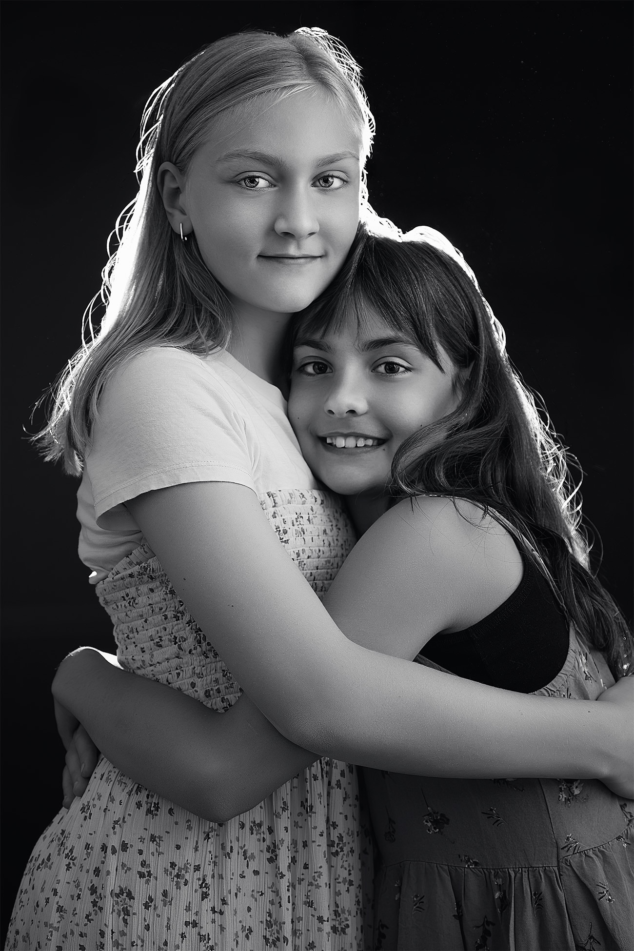 Black and white portrait of two sisters embracing photographed in studio lighting in Surrey BC Black and white portrait of two sisters embracing photographed in studio lighting in Surrey BC