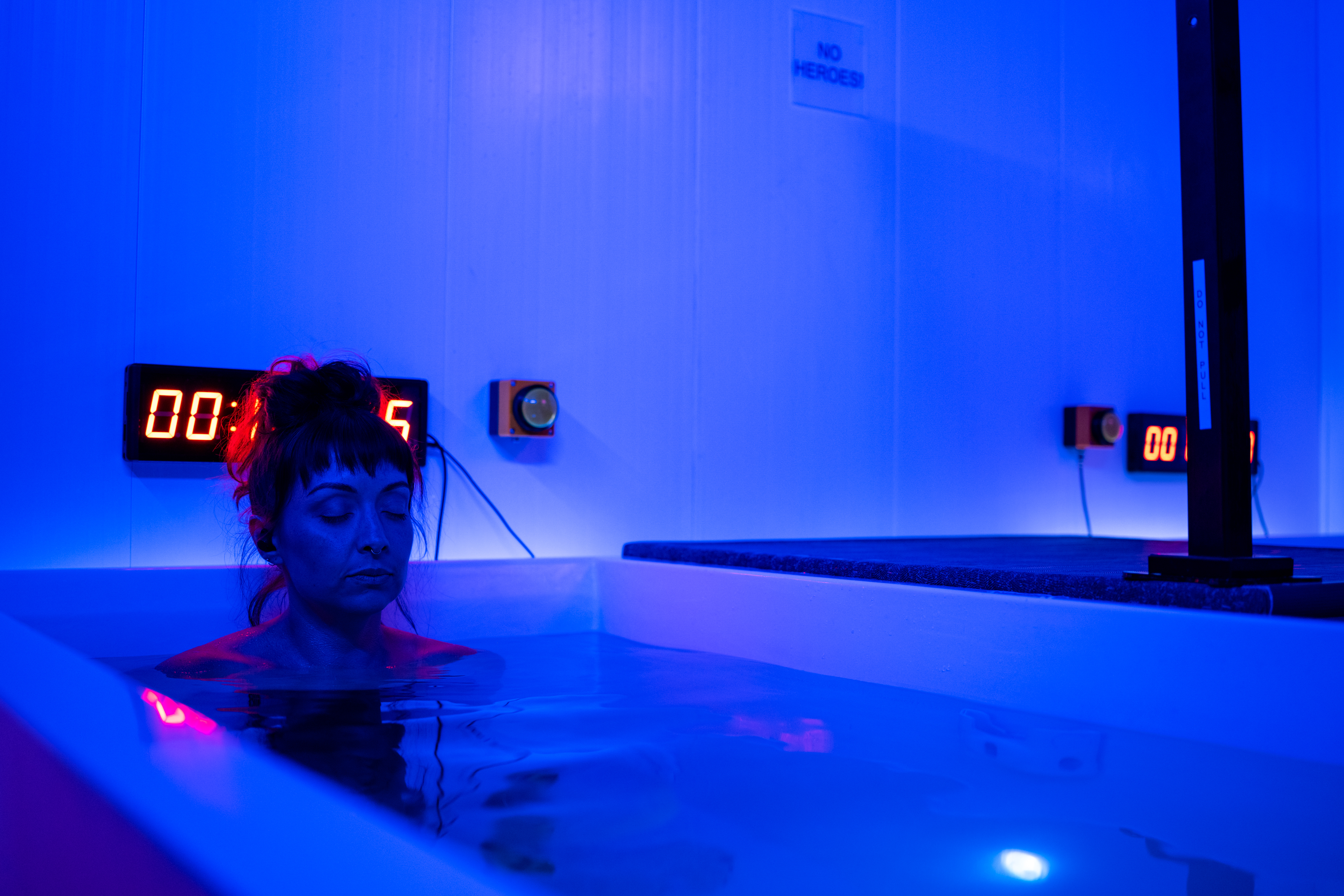 Woman posing confidently in blue-lit cold plunge room at Evolve
