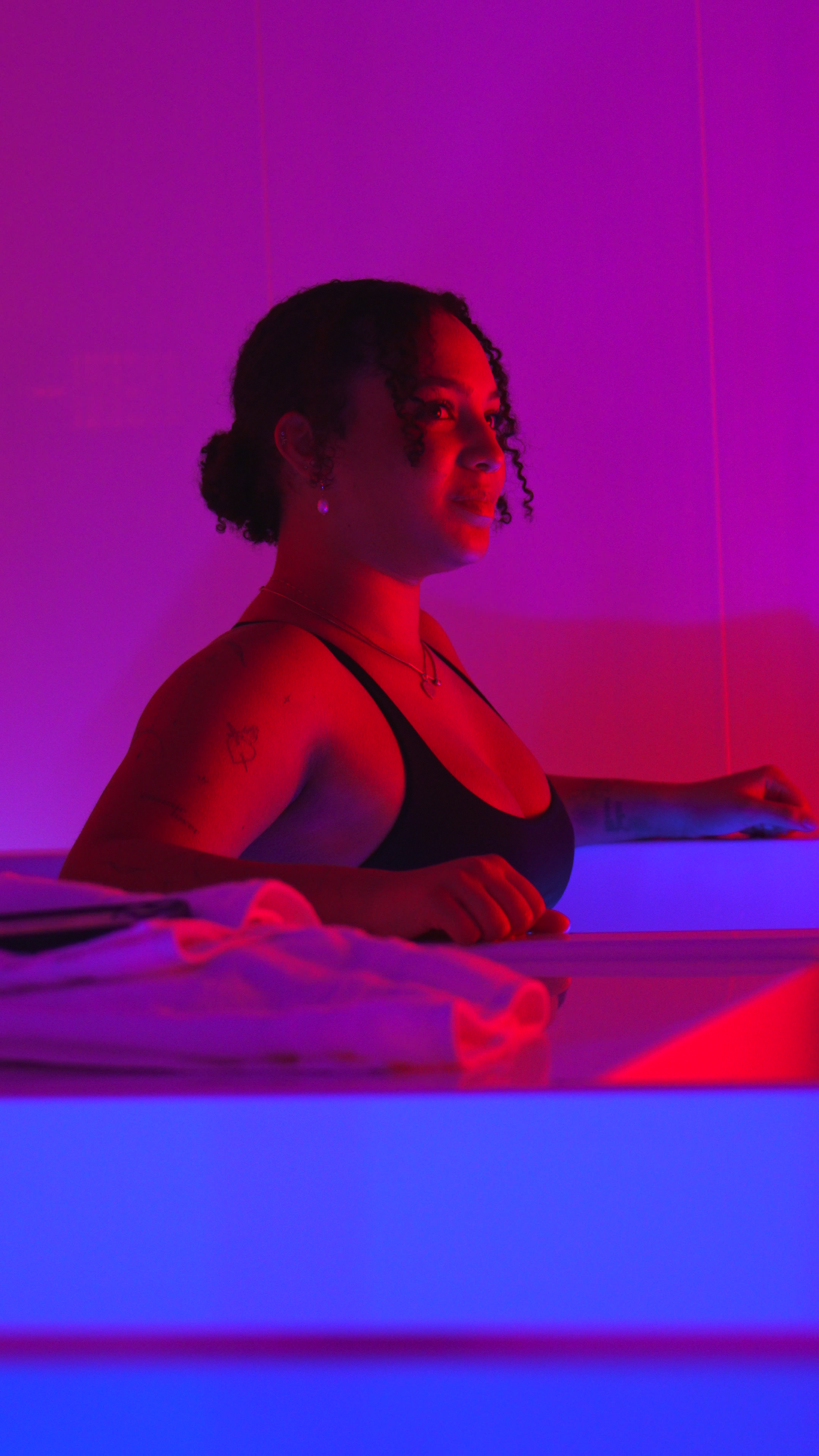 Woman in cold plunge with red and blue ambient lighting at Evolve